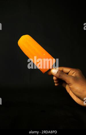 Glace orange à la main sur fond noir, gros plan de photo Banque D'Images