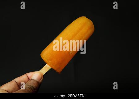 Glace orange à la main sur fond noir, gros plan de photo Banque D'Images