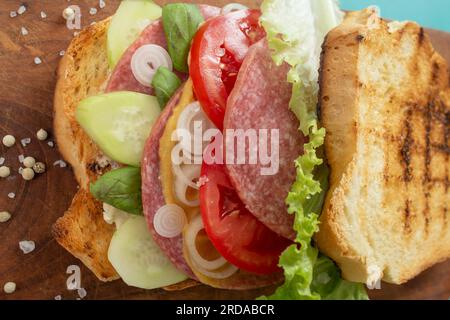 tranches de pain grillées avec concombre, oignon, tomates, laitue et salami, sandwich sur une planche à découper en bois, texture douce et rapprochée Banque D'Images