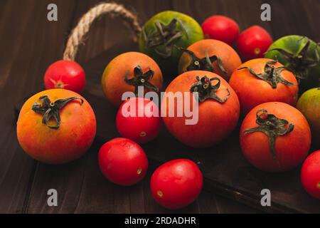 Collection de tomates entières colorées servies sur un fond rustique en bois, tomatos nature morte Banque D'Images