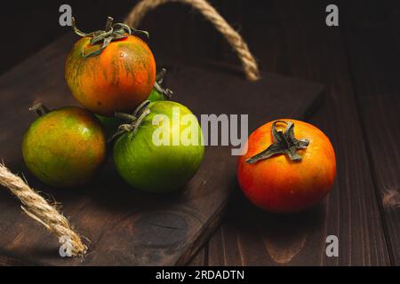 Collection de tomates entières colorées servies sur un fond rustique en bois, tomatos nature morte Banque D'Images