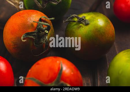 Collection de tomates entières colorées servies sur un fond rustique en bois, tomatos nature morte Banque D'Images