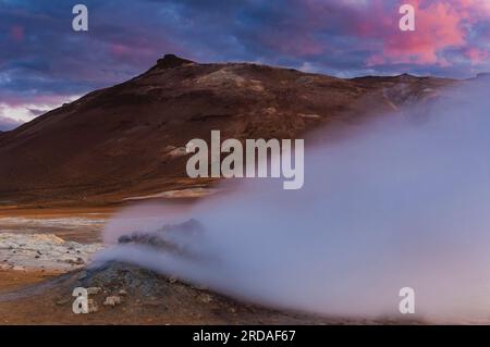 Un magnifique lever de soleil peint le ciel d'oranges vibrantes et de roses sur une zone thermale volcanique, avec des geysers, des montagnes et des mers de nuages. ICEL Banque D'Images