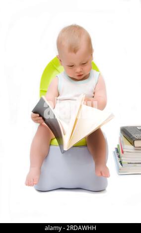 Le petit garçon est assis sur un pot de chambre et lit le livre Banque D'Images