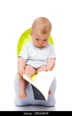 Le petit garçon est assis sur un pot de chambre et lit le livre Banque D'Images