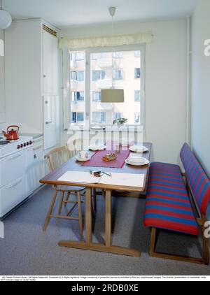 Cuisine dans le passé. Une cuisine avec un coin repas à la fin des années 1950 Il y a de la place pour une plus grande table à manger en bois avec des chaises assorties et un canapé de cuisine. Un réfrigérateur intégré a un placard de rangement au-dessus. Une cuisinière électrique brille d'un blanc vif et une cafetière rouge mijote sur l'une des assiettes. La table est sertie de porcelaine blanche à motifs et un bloc de dessin est étalé sur le coin. Un jouet mécanique est sur la nappe. Suède 1958. Réf. Bv110-6 Banque D'Images