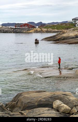 Femme debout sur les rochers regardant la mère de la mer, Sassuma Arnaa, sculpture de Christian Rosing à Nuuk, Groenland en juillet Banque D'Images
