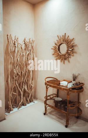 Plan vertical d'une maison rustique à Barcelone. Les murs beiges, les éléments en bois et le miroir créent de la chaleur. Une table basse en rotin avec des objets décoratifs, Banque D'Images