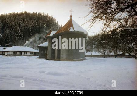 Monastère de Tarcau, comté de Neamt, Roumanie, 1999. Vue extérieure de l'église en bois, construite en 1833. Scène hivernale, avec de la neige couvrant le sol et de la fumée sortant de la cheminée d'une cellule monastique. Banque D'Images