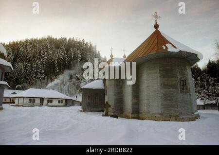 Monastère de Tarcau, comté de Neamt, Roumanie, 1999. Vue extérieure de l'église en bois, construite en 1833. Scène hivernale, avec de la neige couvrant le sol et de la fumée sortant de la cheminée d'une cellule monastique. Banque D'Images