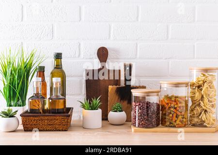 diverses bouteilles d'huile pour la cuisson et bocaux en verre pour les produits en vrac, planches à découper et plantes vertes à l'intérieur de la cuisine. vue avant Banque D'Images