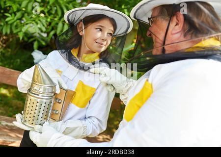 Fille apprenant sur le fumeur de l'apiculteur mâle senior au jardin de rucher Banque D'Images