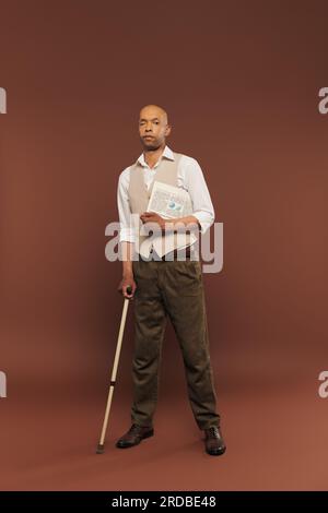 inclusion, homme afro-américain audacieux avec le syndrome de myasthénie grave, debout avec le journal et la canne marchante, homme à la peau foncée avec la maladie chronique Banque D'Images