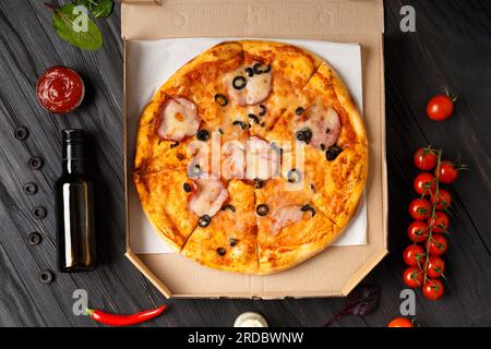 Pizza dans une boîte ouverte, sauces, légumes frais sur un fond en bois foncé. Livraison de pizza Banque D'Images