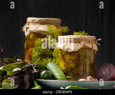 Concombres marinés dans un bocal, salade de concombre tranché en conserve, cornichons frais, herbes et épices sur un fond sombre, gros plan. Banque D'Images