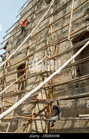 Île de Cebu, Philippines-27 janvier 2023 : utilisant de façon précaire des poteaux de bambou comme plate-forme de travail et portant des tongs, les ouvriers appliquent de la whitewa Banque D'Images