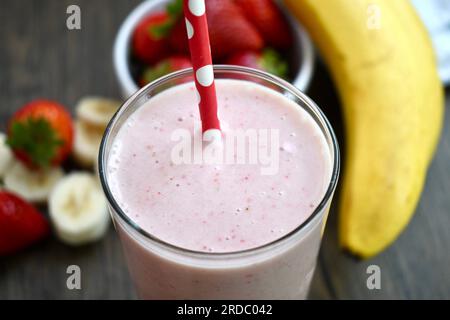 Smoothie banane fraise dans un verre transparent sur une table en bois Banque D'Images
