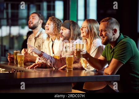 Des gens joyeux, des amis assis dans le bar, regardant attentivement la traduction de match de football, boire, ing bière, s'amuser Banque D'Images