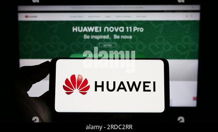 Personne tenant le téléphone portable avec le logo de la société chinoise Huawei technologies Co. Ltd. Sur l'écran en face de la page Web. Concentrez-vous sur l'affichage du téléphone. Banque D'Images