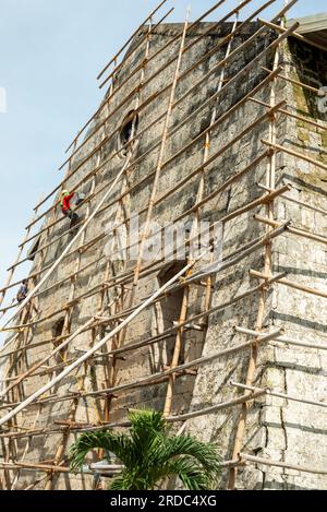 Île de Cebu, Philippines-27 janvier 2023 : utilisant des poteaux de bambou comme échafaudage et portant des tongs sur ses pieds, l'ouvrier applique de la peinture blanche t Banque D'Images