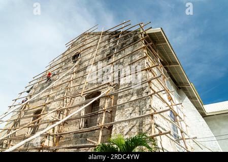 Île de Cebu, Philippines-27 janvier 2023 : utilisant des poteaux de bambou comme échafaudage et portant des tongs sur ses pieds, l'ouvrier applique de la peinture blanche t Banque D'Images