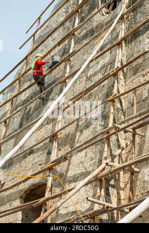 Île de Cebu, Philippines-27 janvier 2023 : utilisant des poteaux de bambou comme échafaudage et portant des tongs sur ses pieds, l'ouvrier applique de la peinture blanche t Banque D'Images