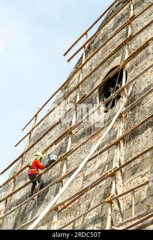 Île de Cebu, Philippines-27 janvier 2023 : utilisant des poteaux de bambou comme échafaudage et portant des tongs sur ses pieds, l'ouvrier applique de la peinture blanche t Banque D'Images