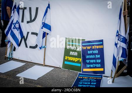 Tel Aviv, Israël. 19 juillet 2023. Des pancartes en hébreu indiquant « nous ne servirons pas sous une dictature (L), et « le gouvernement d'Israël vous avez rompu le contrat avec les soldats de réserve » sont vues à côté du drapeau israélien lors d'une manifestation à tel Aviv. Un plan controversé du gouvernement visant à réformer le système judiciaire du pays a brisé de profondes divisions au sein de la société israélienne. Ces divisions ont infiltré les forces armées, où les réservistes des unités stratégiques clés se sont engagés à ne pas se présenter à la réserve si les changements législatifs sont poussés à adopter. Crédit : SOPA Images Limited/Alamy Live News Banque D'Images