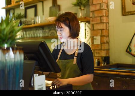 Jeune serveuse vietnamienne travaillant avec la machine de check out dans le café Banque D'Images