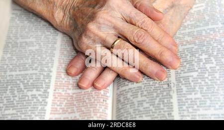 Les vieilles mains s'attachent ensemble au-dessus d'une Bible ouverte. Les mains sont froissées et portées avec les soucis du monde. Banque D'Images