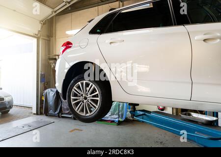 Centre de service de voiture. Bas derrière le véhicule pov soulevé sur le technicien de levage travailleur effectuer des diagnostics et l'inspection au poste de maintenance . Automobile Banque D'Images