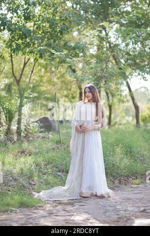 Belle fille asiatique posant devant les arbres et donnant la pose. Le ventre de la fille est révélateur et porte robe blanche de robe orientale Banque D'Images