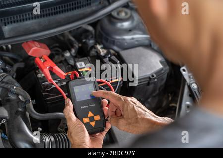 Fermez les mains d'un mécanicien automobile masculin utilisant un testeur de batterie pour tester l'état de la batterie de la voiture Banque D'Images