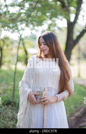 Belle fille asiatique posant devant les arbres et donnant la pose. Le ventre de la fille est révélateur et porte robe blanche de robe orientale Banque D'Images