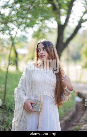 Belle fille asiatique posant devant les arbres et donnant la pose. Le ventre de la fille est révélateur et porte robe blanche de robe orientale Banque D'Images