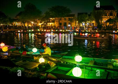 Des bateliers vietnamiens attendent les passagers la nuit alors que d'autres bateaux touristiques illuminés par des lanternes naviguent sur la rivière Thu bon à Hoi an, Vietnam. Banque D'Images