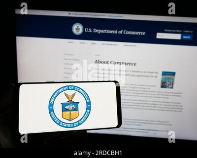 Personne tenant un smartphone avec le sceau du Département du Commerce des États-Unis (DOC) sur l'écran devant le site Web. Concentrez-vous sur l'affichage du téléphone. Banque D'Images
