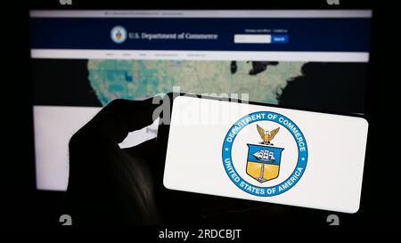 Personne tenant un téléphone portable avec le sceau du Département du Commerce des États-Unis (DOC) sur l'écran devant la page Web. Concentrez-vous sur l'affichage du téléphone. Banque D'Images
