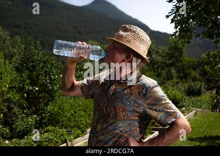 Briançon, France. 20 juillet 2023. Un homme de 73 ans travaille dans son potager. Il boit de l'eau dans une bouteille pour rester hydraté, France le 20 juillet 2023. Ilustration de l'importance de l'hydratation chez le sujet âgé en période de forte chaleur ou de vagues de chaleur. Photo de Thibaut Durand/ABACAPRESS.COM crédit : Abaca Press/Alamy Live News Banque D'Images