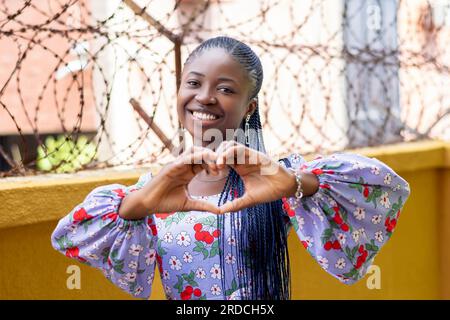 Photo d'une femme africaine joyeuse créant une forme de cœur avec ses mains, exprimant l'excitation et l'amour Banque D'Images