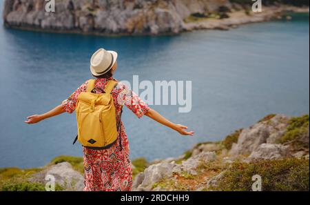 Femme asiatique en chapeau regarder sur les vues de la baie d'azur dans la mer Méditerranée. Concept de voyage et de vacances. Baie Anthony Quinn avec eau cristalline sur l'île de Rhodes, Grèce. La plus belle plage. Banque D'Images