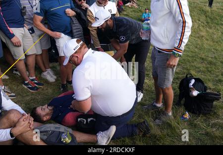 L'Espagnol Jon Rahm marche au-dessus d'un fan qui a été frappé par un tir de tee-shirt décalé pendant la première journée de l'Open au Royal Liverpool, Wirral. Date de la photo : jeudi 20 juillet 2023. Banque D'Images