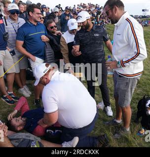 L'Espagnol Jon Rahm marche au-dessus d'un fan qui a été frappé par un tir de tee-shirt décalé pendant la première journée de l'Open au Royal Liverpool, Wirral. Date de la photo : jeudi 20 juillet 2023. Banque D'Images