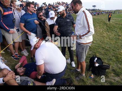 L'Espagnol Jon Rahm marche au-dessus d'un fan qui a été frappé par un tir de tee-shirt décalé pendant la première journée de l'Open au Royal Liverpool, Wirral. Date de la photo : jeudi 20 juillet 2023. Banque D'Images