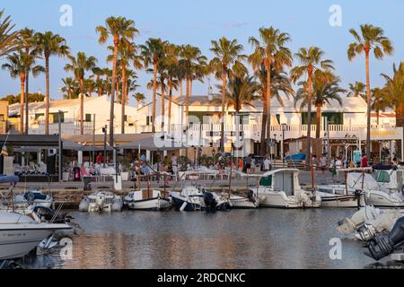 Les touristes profitent des terrasses le long du port dans la station balnéaire de Cala en Bosc sur l'île espagnole de Minorque. Banque D'Images