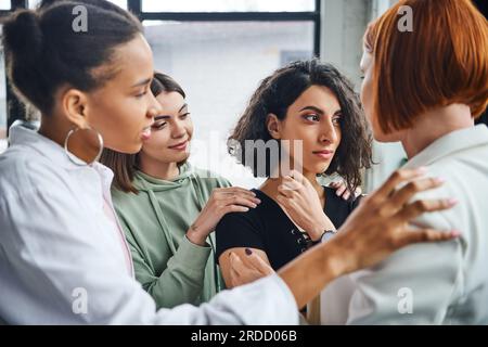 femme multiraciale offensée regardant loin près des amies féminines multiculturelles et psychologue la calmant dans la salle de consultation, la résolution de problèmes et mutuelle Banque D'Images