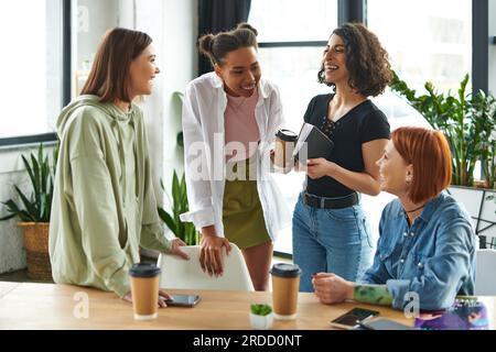 joyeuse amies multiraciales et afro-américaines avec cahier et boisson à emporter riant près des femmes positives dans le club d'intérêt, rassemblement heureux Banque D'Images