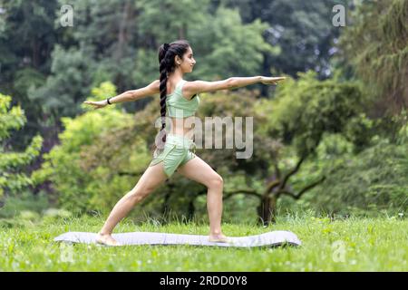 Jeune belle femme dans le parc sur un tapis de sport faisant du fitness et faisant des exercices sportifs actifs, femme hindoue faisant du yoga dans le parc le matin parmi les arbres, s'étirant et méditant. Banque D'Images