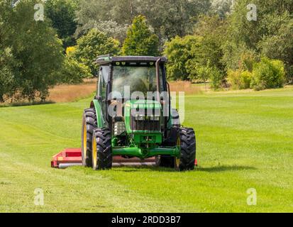 Tracteur coupant l'herbe dans un parc de campagne par une journée ensoleillée en été. ROYAUME-UNI Banque D'Images