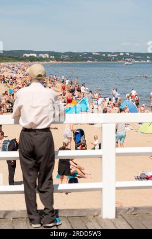 Homme senior debout sur la jetée regardant les amateurs de plage bronzer à la plage de Brzezno, Gdansk, Pologne Banque D'Images